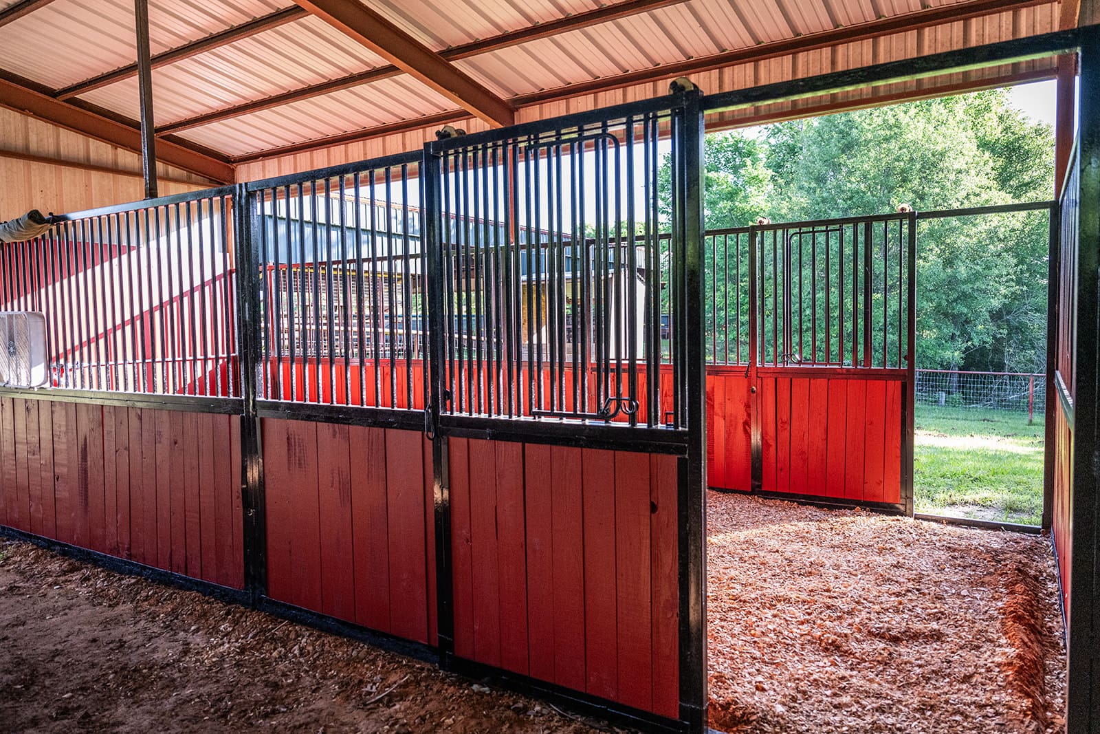 Clean and spacious horse stable with red wooden panels and metal bars.