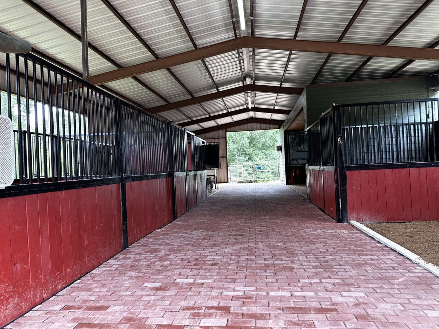 Interior view of a horse stable with brick flooring and metal gates.