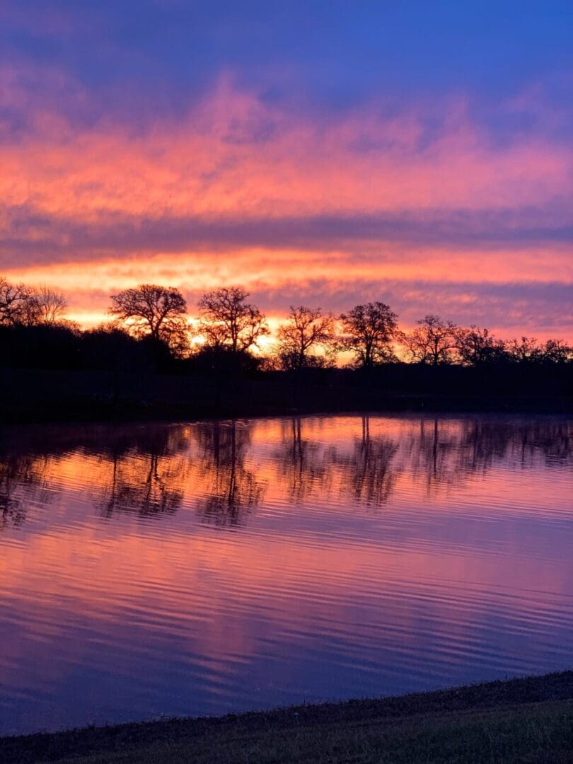 Sunset with vibrant pink and purple sky reflected on calm water.